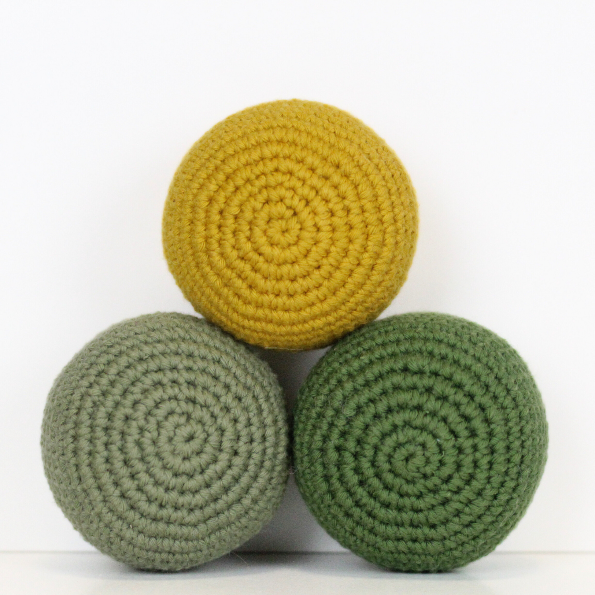 Three crocheted balls in forest green, moss green, and mustard yellow. Handmade crochet dog toys from Lana Royals Pet Wear.
