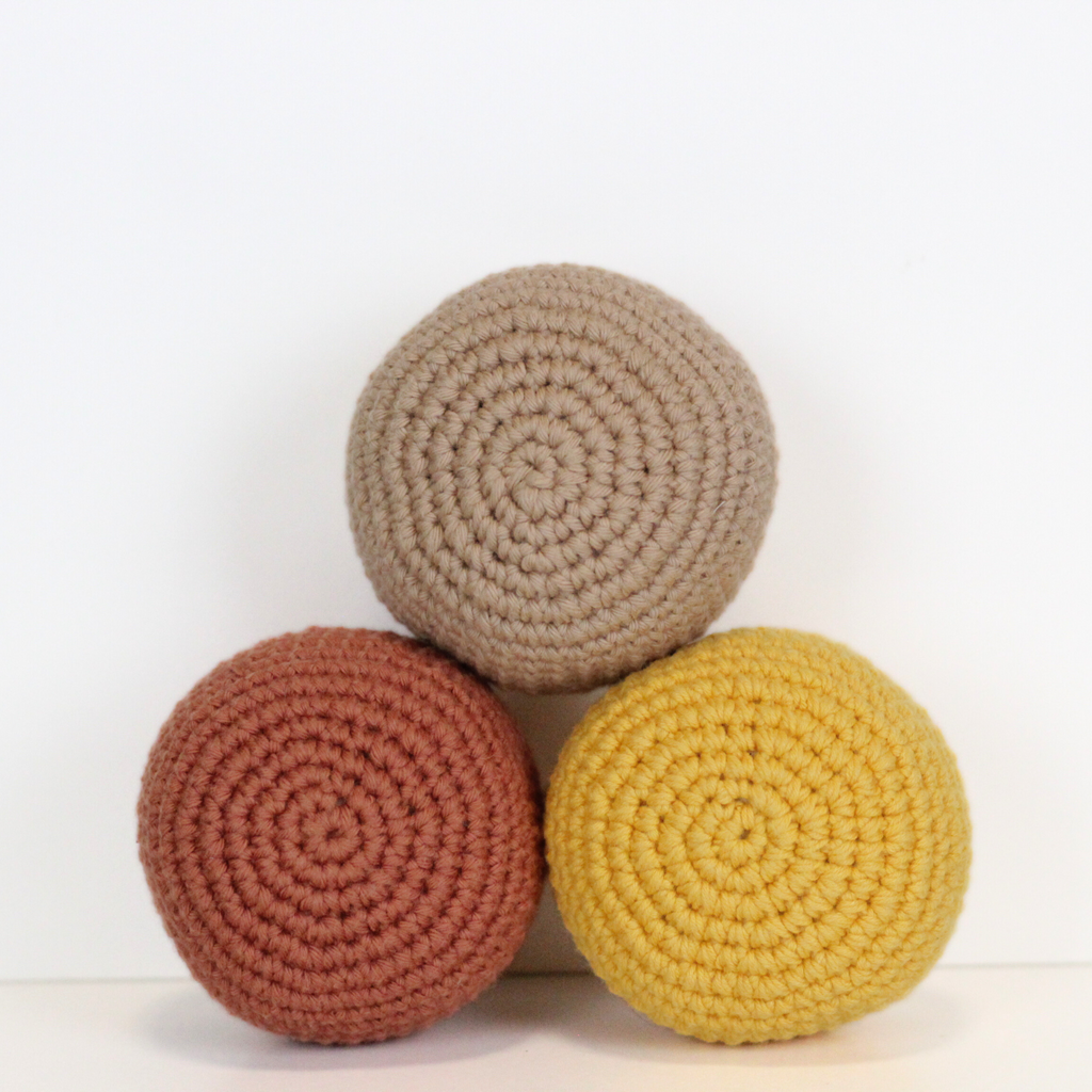 Three crocheted balls in beige, orange rust, and dandelion yellow. Three crocheted balls in forest green, moss green, and mustard yellow. Handmade crochet dog toys from Lana Royals Pet Wear.