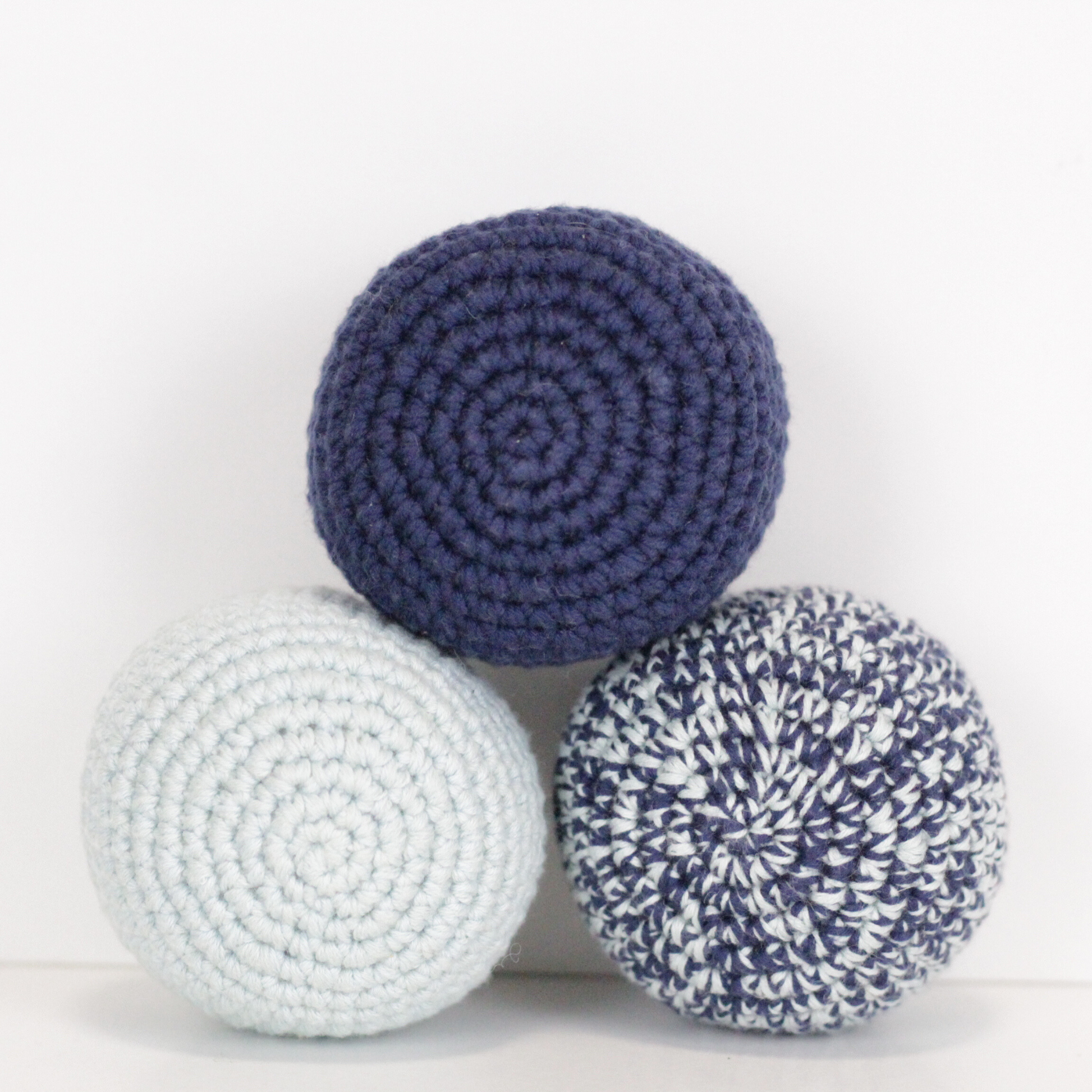 Three crocheted balls in merle blue, baby blue and navy blue. Handmade crochet dog toys from Lana Royals Pet Wear.