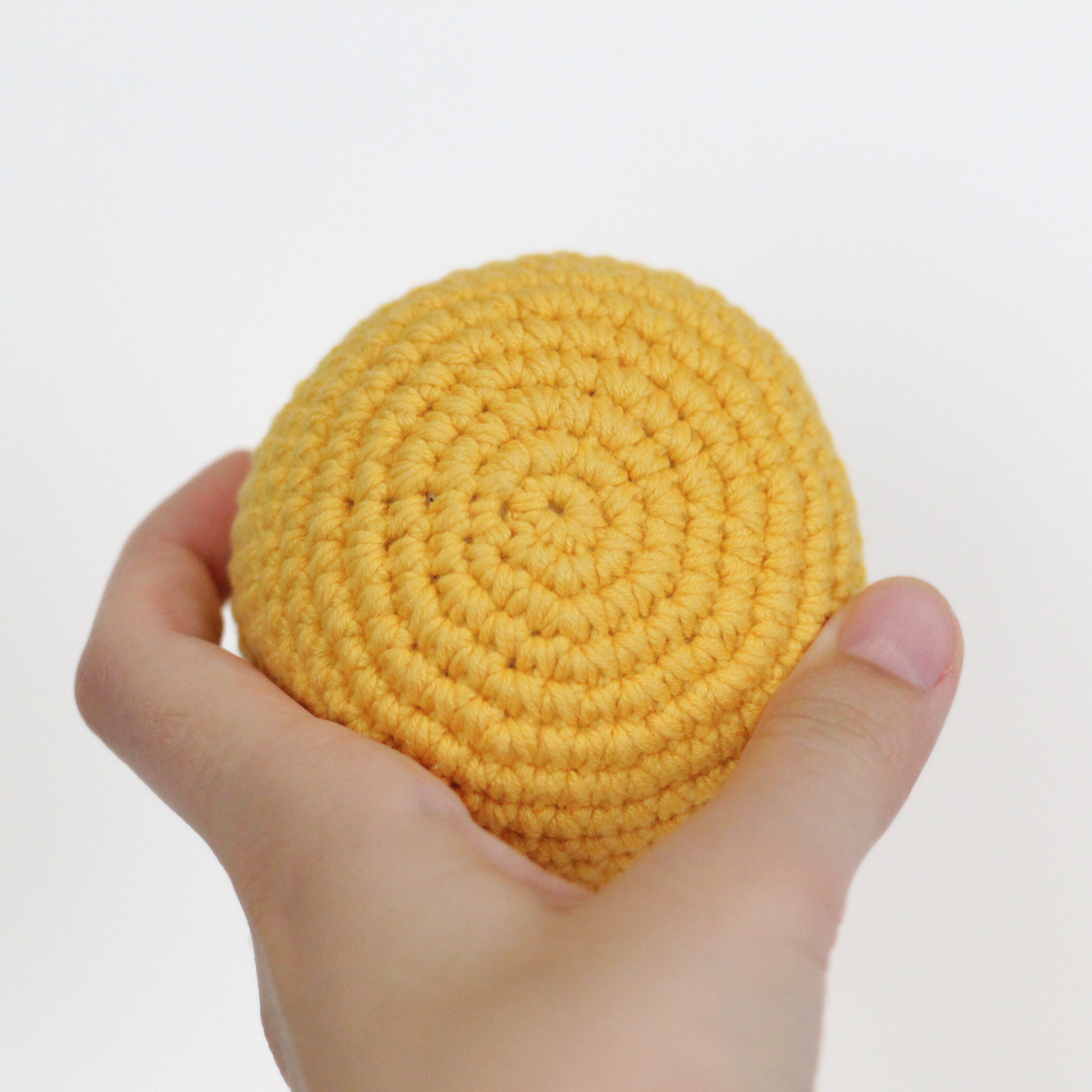 Yellow crocheted ball held in a hand. Handmade crochet dog toys from Lana Royals Pet Wear.