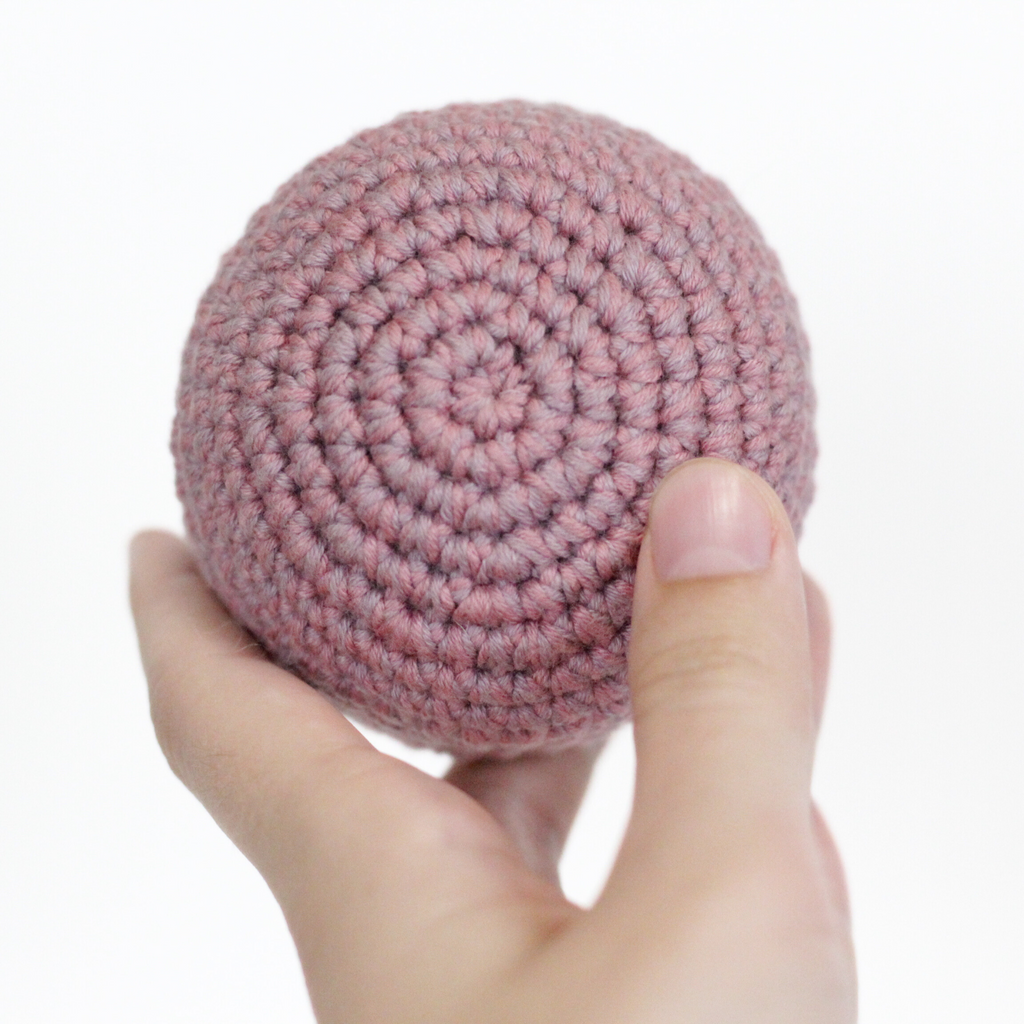Pink crocheted ball held in a hand. Handmade crochet dog toys from Lana Royals et Wear.