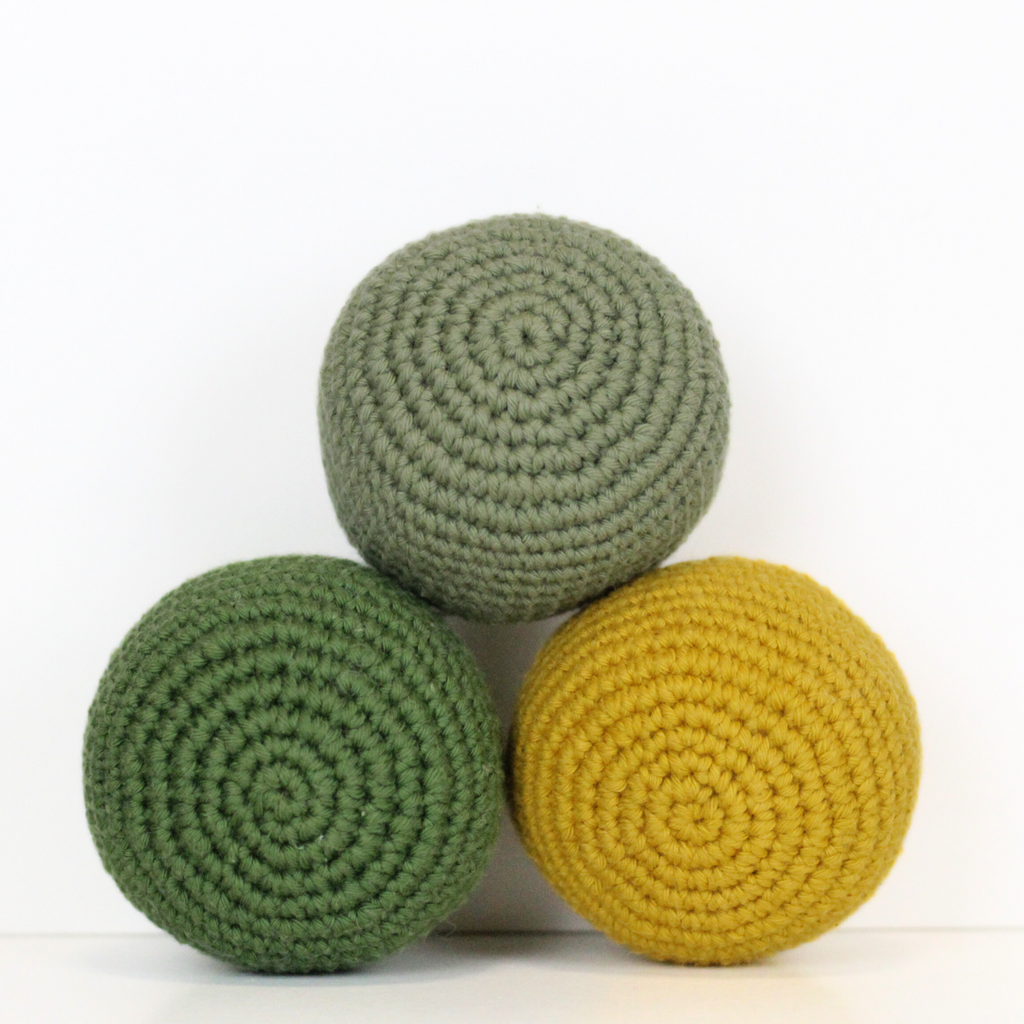 Three crocheted balls in forest green, moss green, and mustard yellow. Handmade crochet dog toys from Lana Royals Pet Wear.
