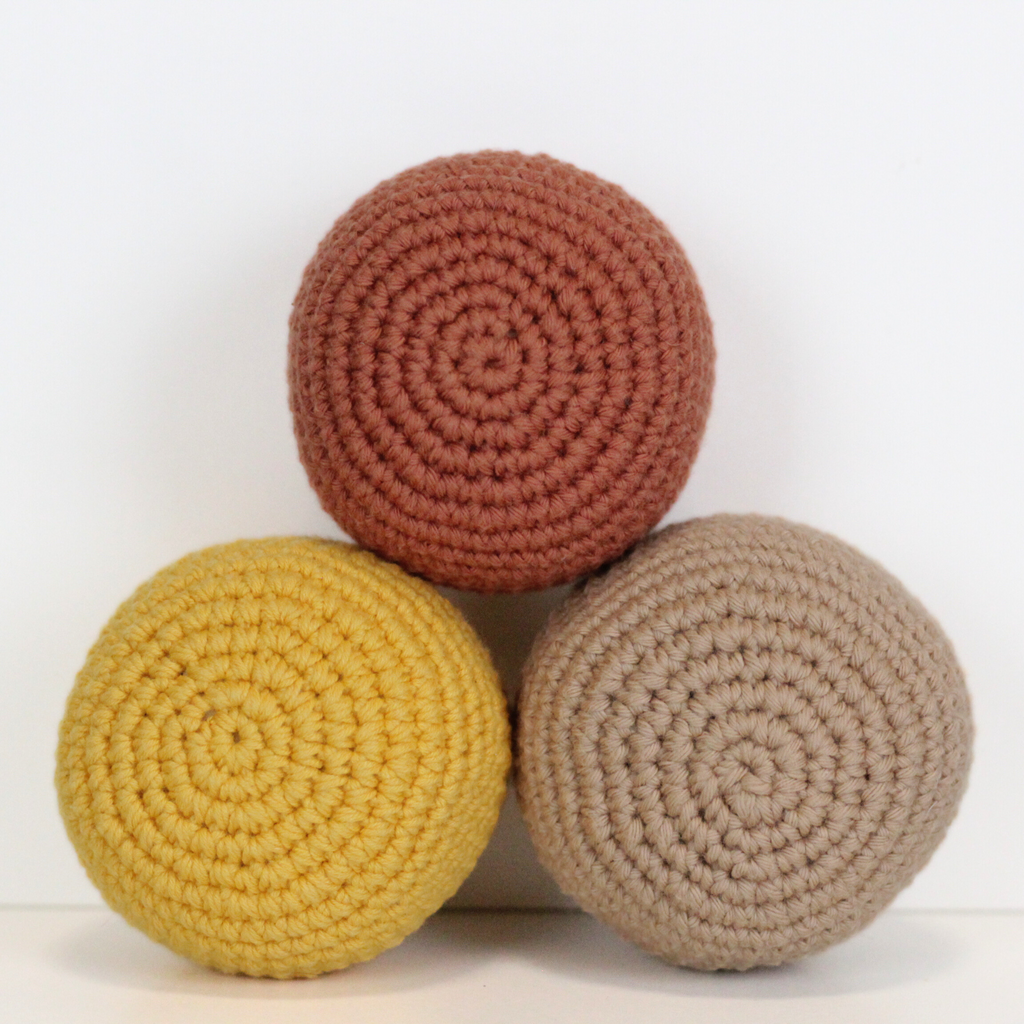 Three crocheted balls in beige, orange rust, and dandelion yellow. Three crocheted balls in forest green, moss green, and mustard yellow. Handmade crochet dog toys from Lana Royals Pet Wear.