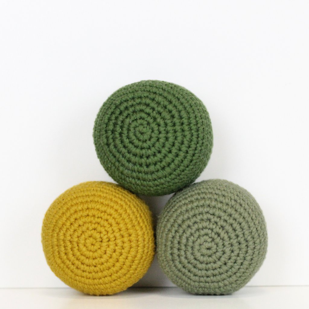 Three crocheted balls in forest green, moss green, and mustard yellow. Handmade crochet dog toys from Lana Royals Pet Wear.