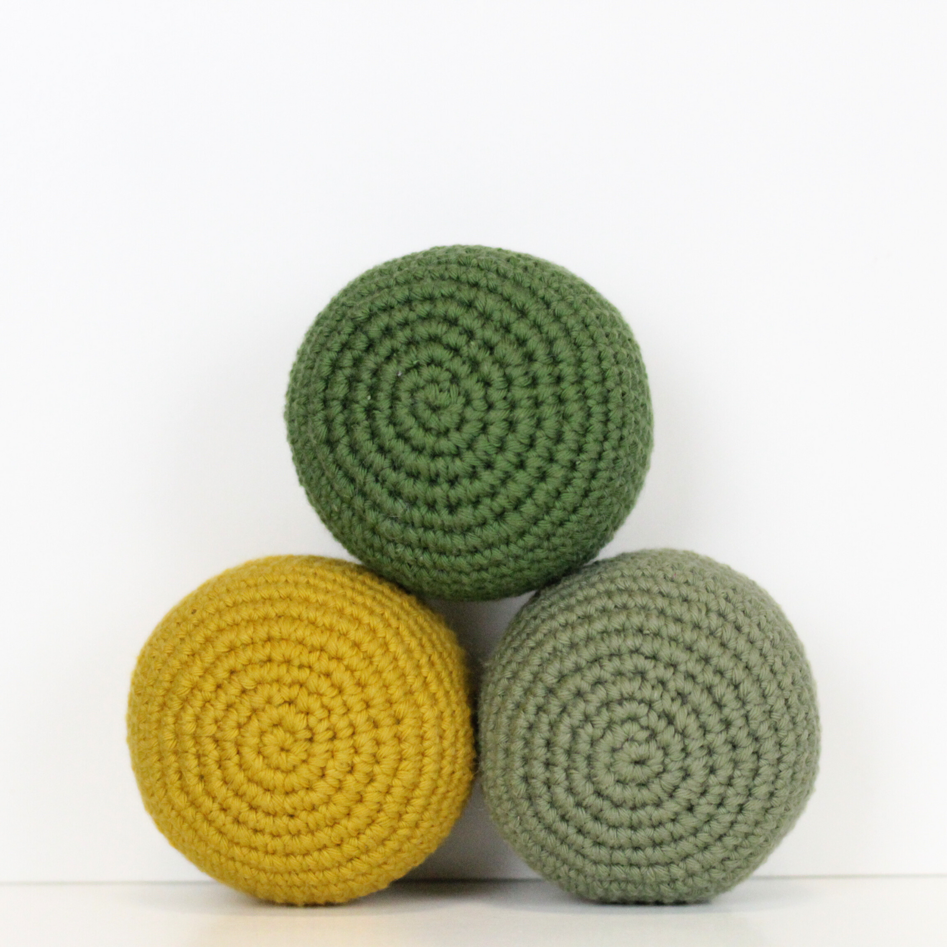 Three crocheted balls in forest green, moss green, and mustard yellow. Handmade crochet dog toys from Lana Royals Pet Wear.