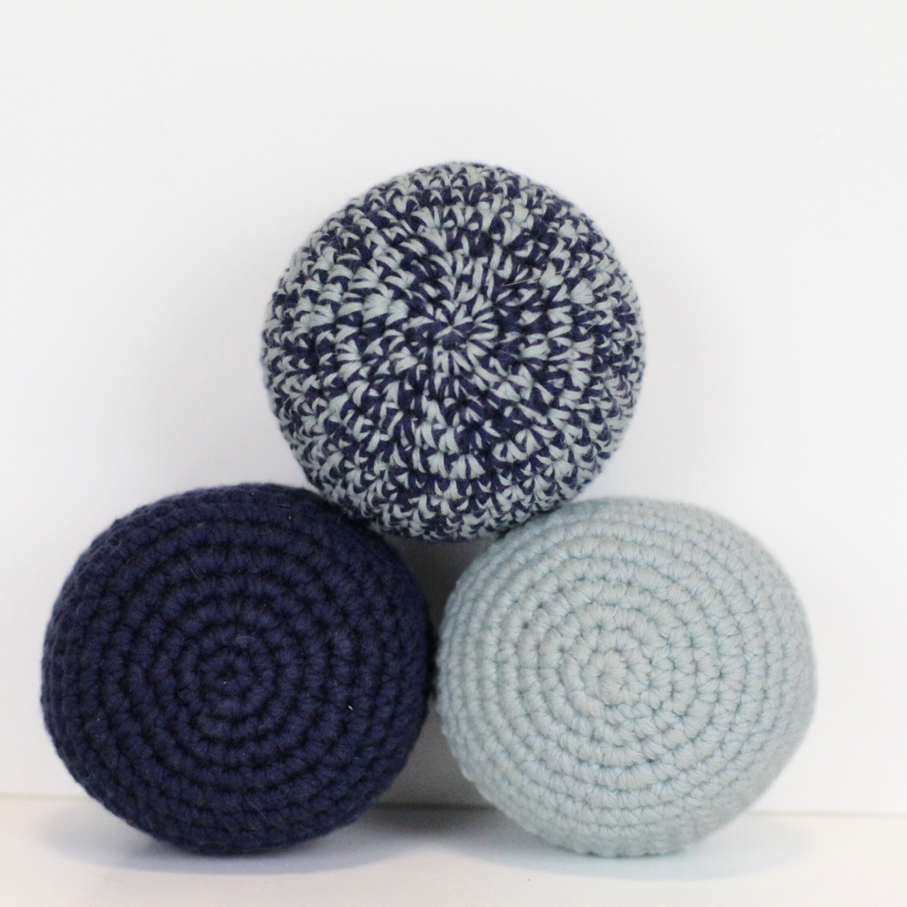 Three crocheted balls in navy blue, merle blue, and light blue. Handmade crochet dog toys from Lana Royals Pet Wear.