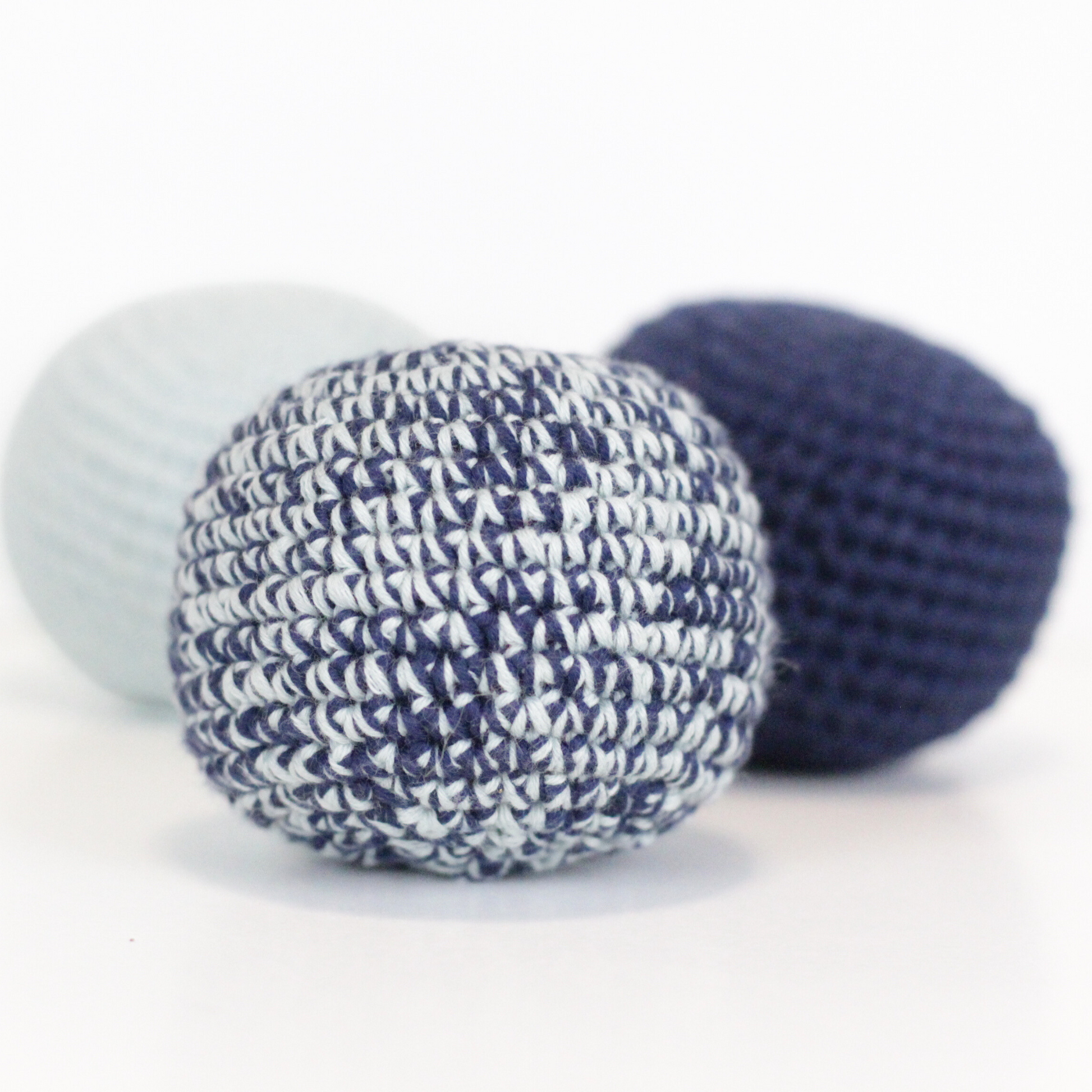 Three crochet balls in merle blue, baby blue, and navy blue. Handmade crochet dog toys from Lana Royals Pet Wear.