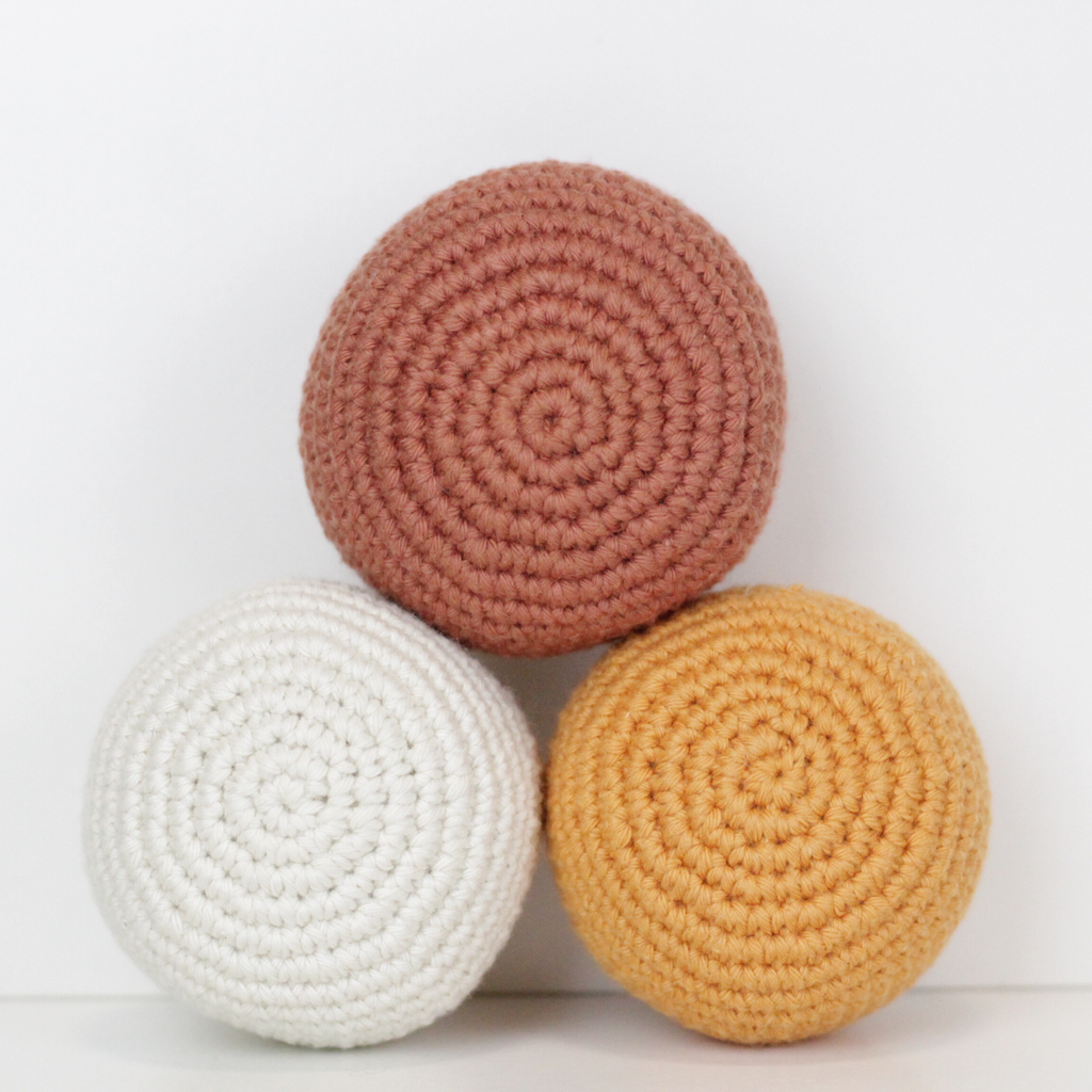 Three crocheted balls in white, rust orange, and apricot yellow. Handmade crochet dog toys from Lana Royals Pet Wear.