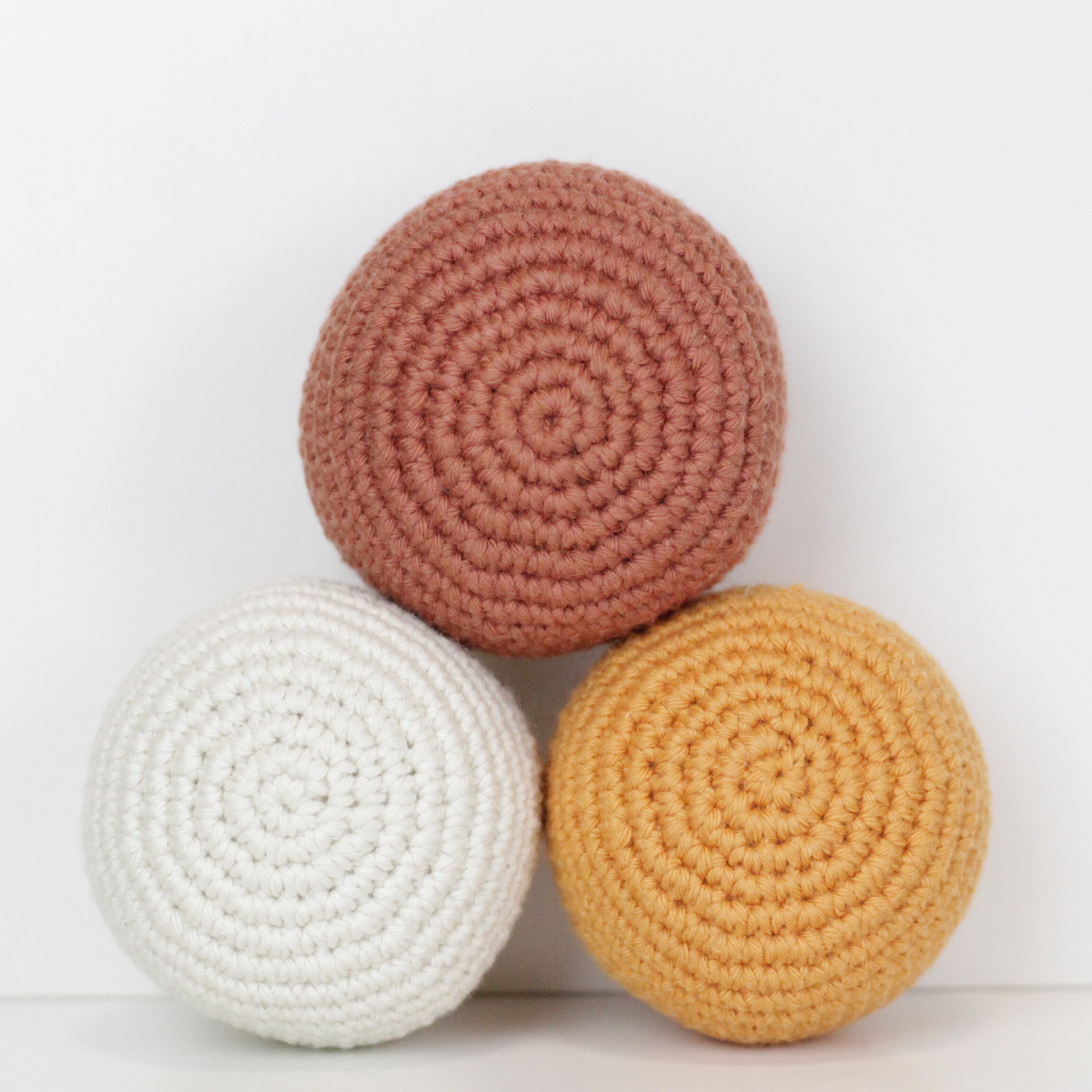 Three crocheted balls in white, rust orange, and apricot yellow. Handmade crochet dog toys from Lana Royals Pet Wear.