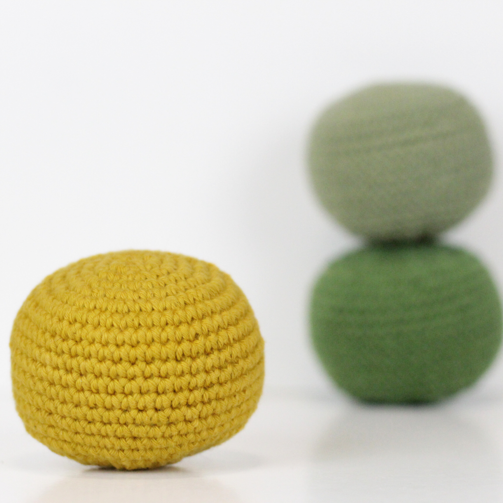 Three crocheted balls in forest green, moss green, and mustard yellow. Handmade crochet dog toys from Lana Royals Pet Wear.