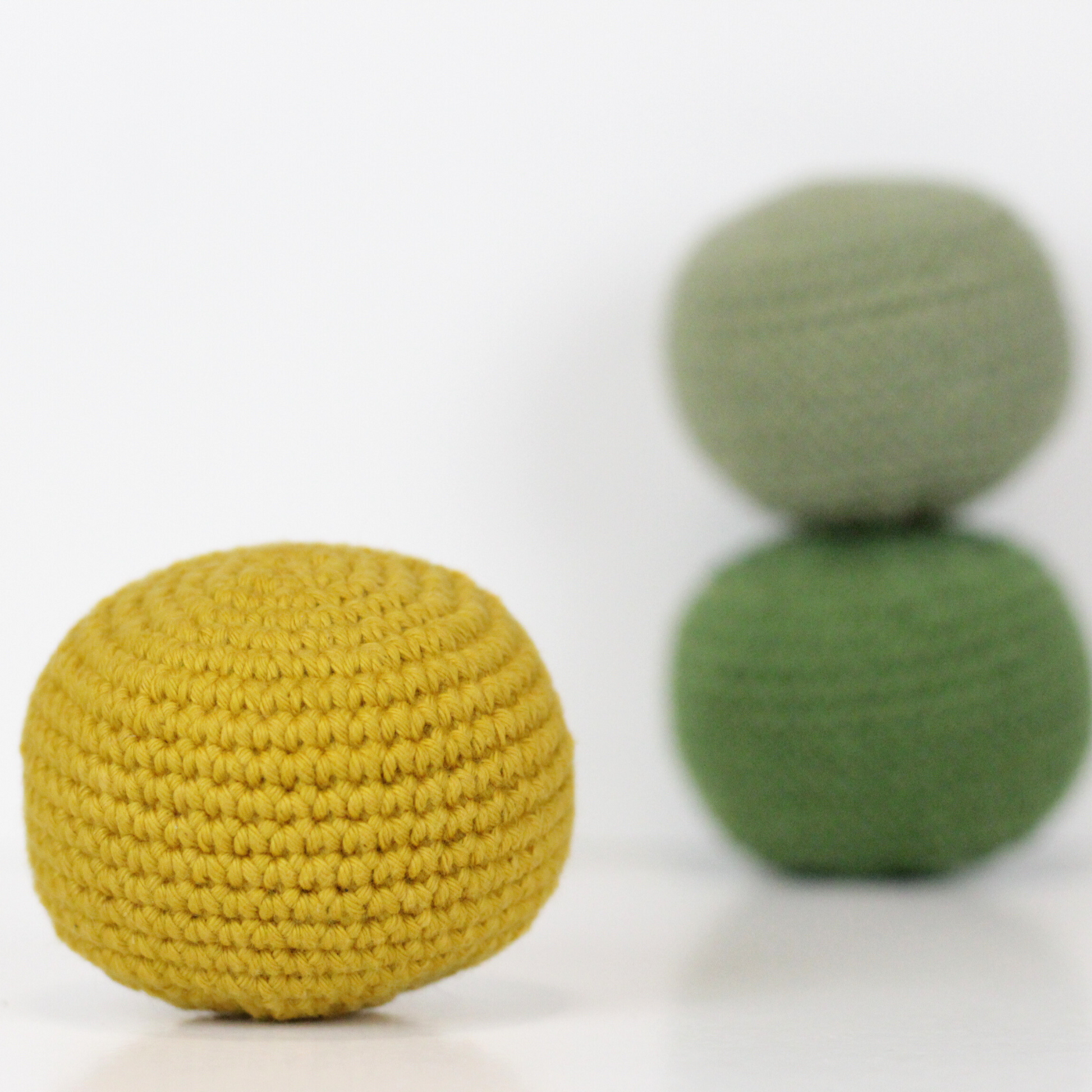 Three crocheted balls in forest green, moss green, and mustard yellow. Handmade crochet dog toys from Lana Royals Pet Wear.