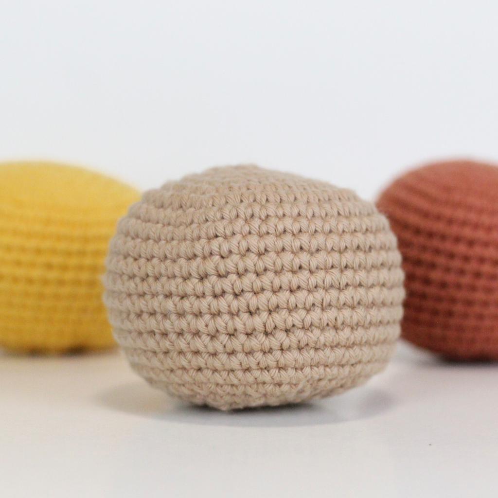 Three crocheted balls in beige, orange rust, and dandelion yellow. Three crocheted balls in forest green, moss green, and mustard yellow. Handmade crochet dog toys from Lana Royals Pet Wear.