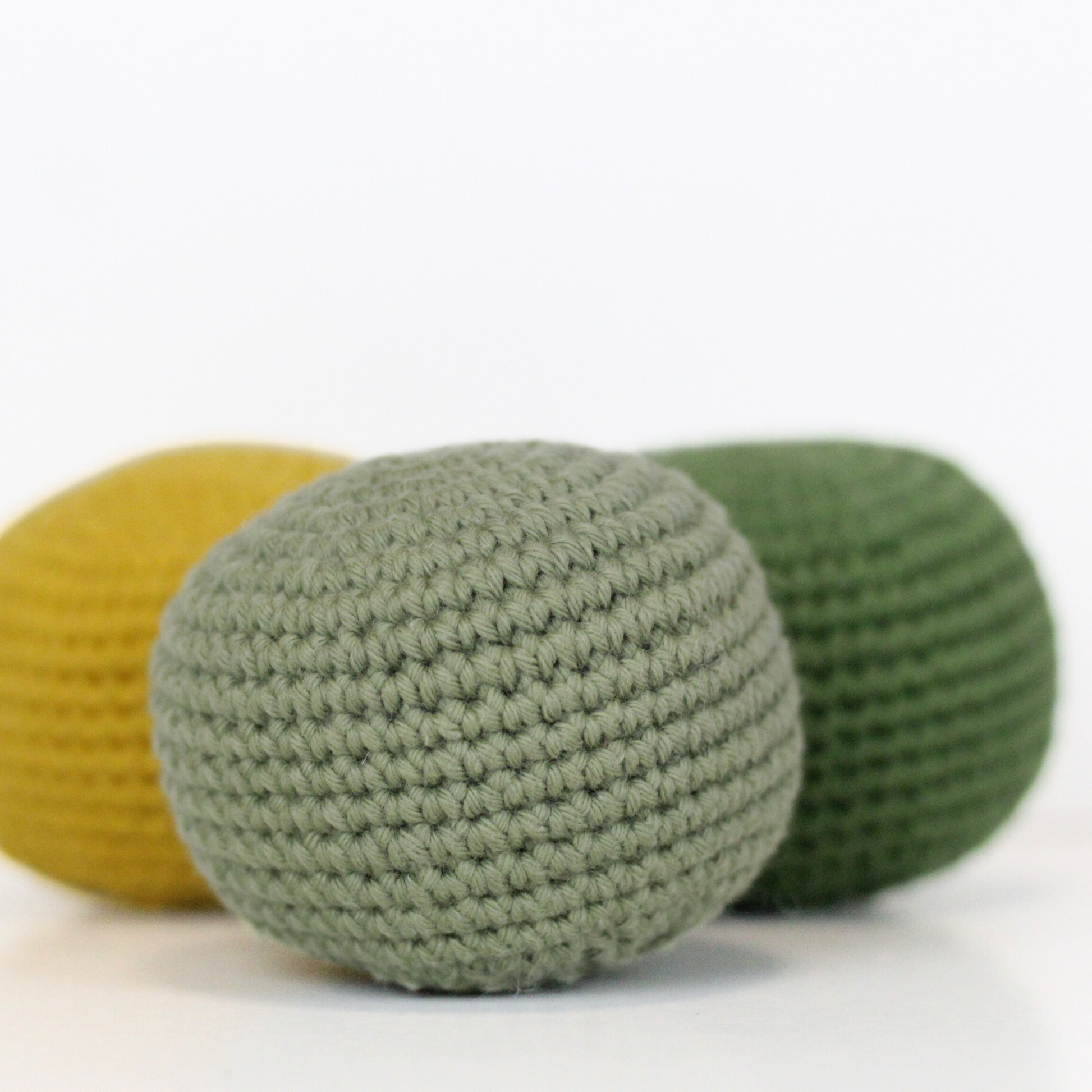 Three crocheted balls in forest green, moss green, and mustard yellow. Handmade crochet dog toys from Lana Royals Pet Wear.