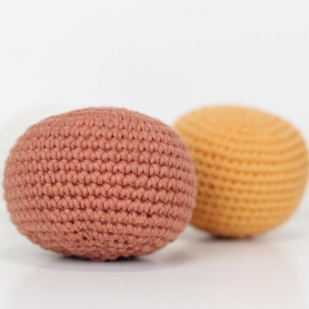 Three crocheted balls in white, rust orange, and apricot yellow. Handmade crochet dog toys from Lana Royals Pet Wear.