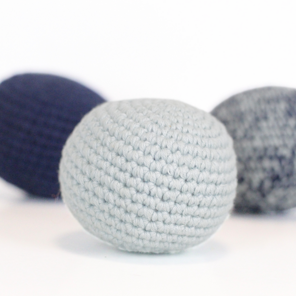 Three crocheted balls in baby blue, merle blue, and navy blue. Handmade crochet dog toys from Lana Royals Pet Wear.