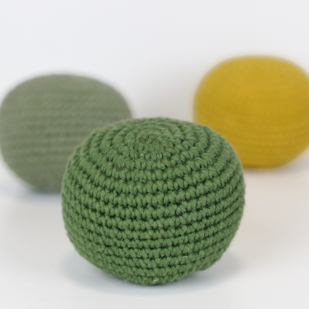 Three crocheted balls in forest green, moss green, and mustard yellow. Handmade crochet dog toys from Lana Royals Pet Wear.