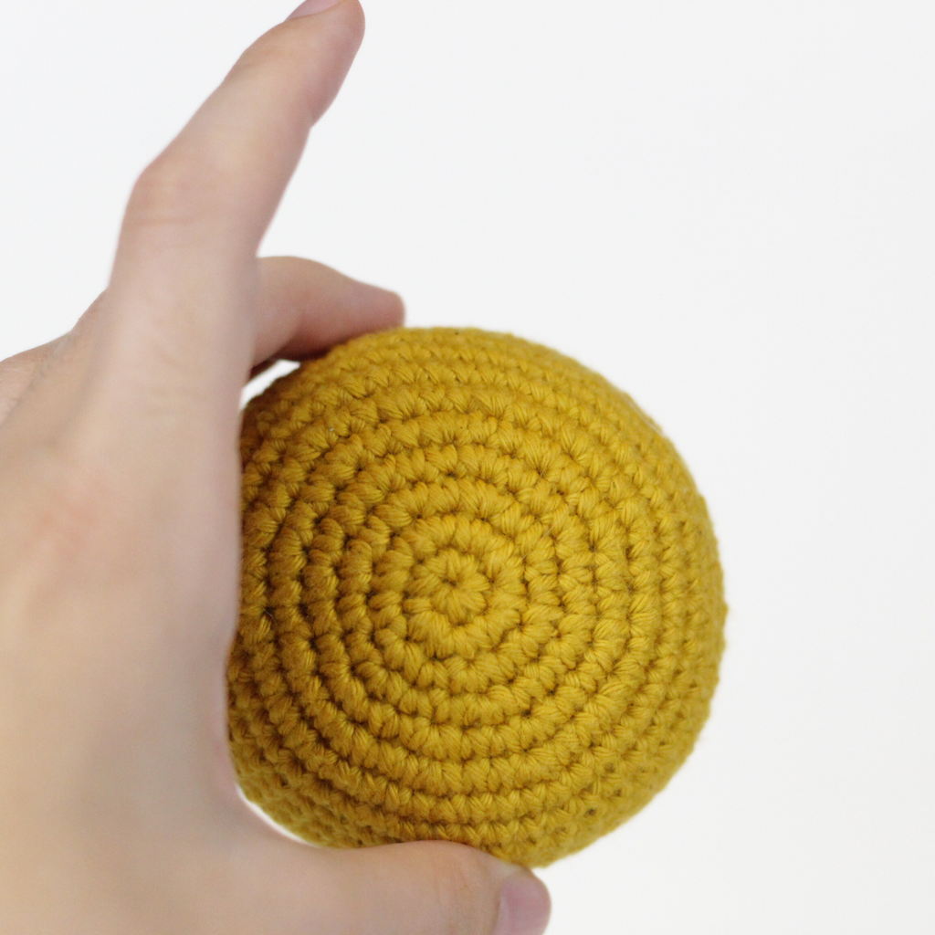 Mustard Yellow crocheted ball held in a hand. Handmade crochet dog toys from Lana Royals Pet Wear.