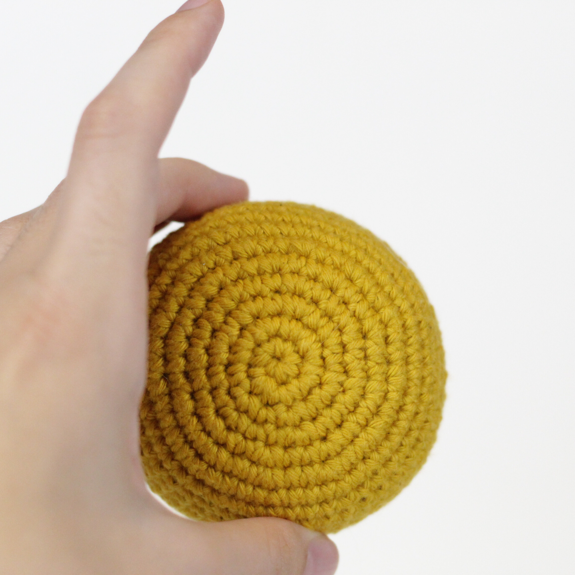 Mustard Yellow crocheted ball held in a hand. Handmade crochet dog toys from Lana Royals Pet Wear.