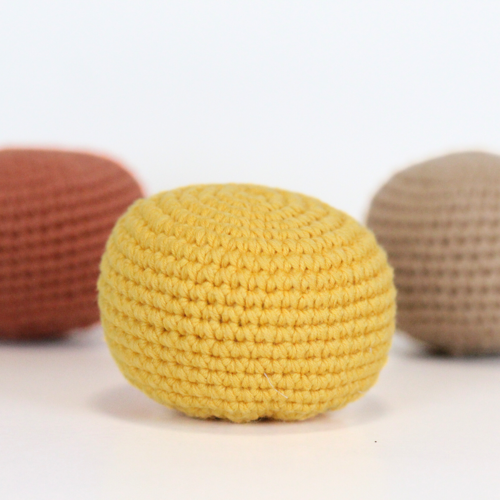Three crocheted balls in beige, orange rust, and dandelion yellow. Three crocheted balls in forest green, moss green, and mustard yellow. Handmade crochet dog toys from Lana Royals Pet Wear.