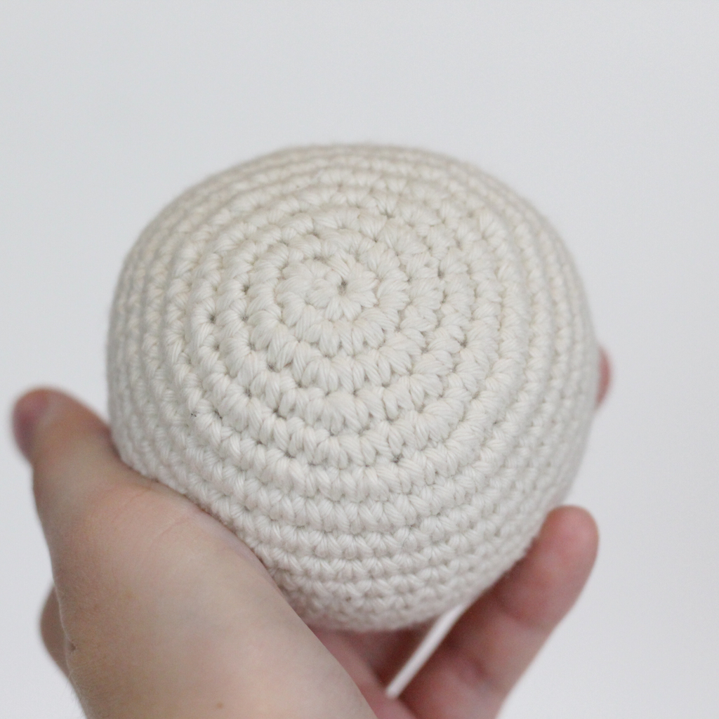 White crocheted ball held in a hand. Handmade crochet dog toys from Lana Royals Pet Wear.