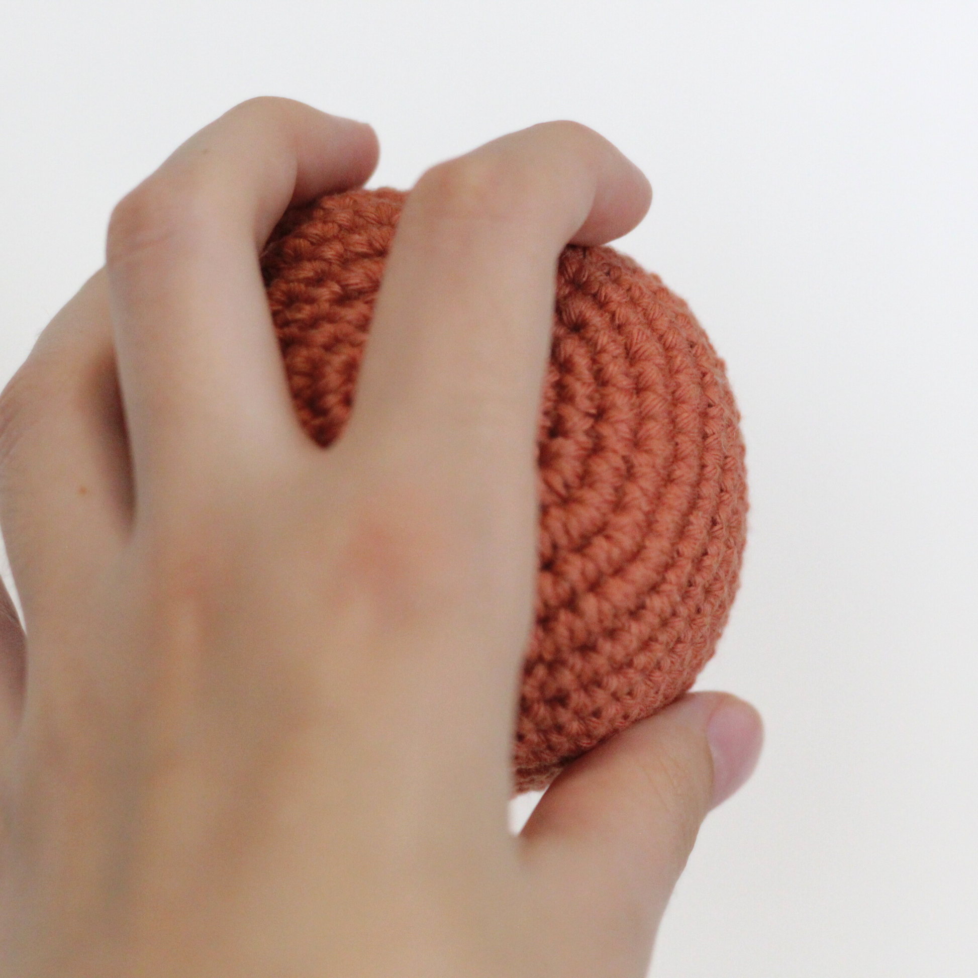Hand holding a rust orange crocheted ball. Handmade crochet dog toys from Lana Royals Pet Wear.