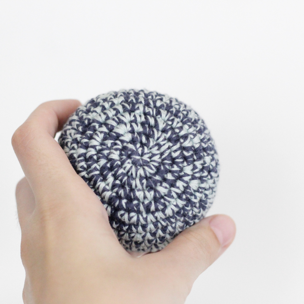 Hand holding a crocheted merle blue ball. Handmade crochet dog toys from Lana Royals Pet Wear.