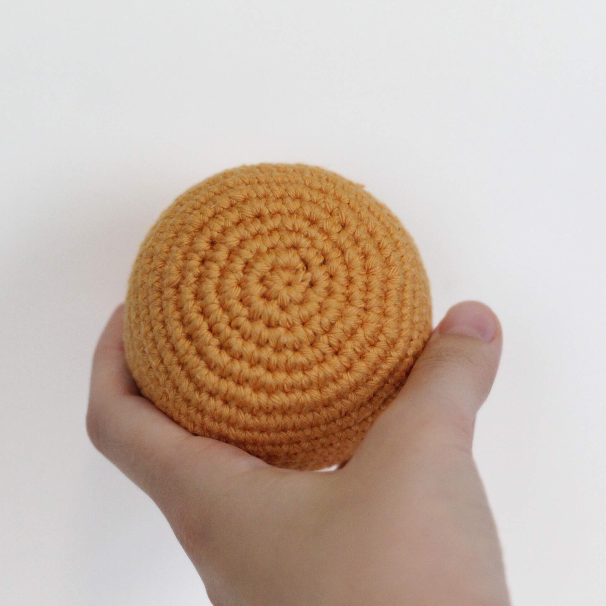 Hand holding a crocheted apricot orange ball. Handmade crochet dog toys from Lana Royals Pet Wear.