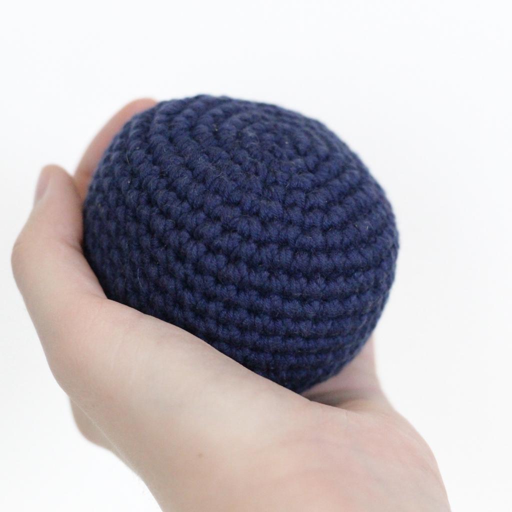 Hand holding a navy blue crocheted ball. Handmade crochet dog toys from Lana Royals Pet Wear.