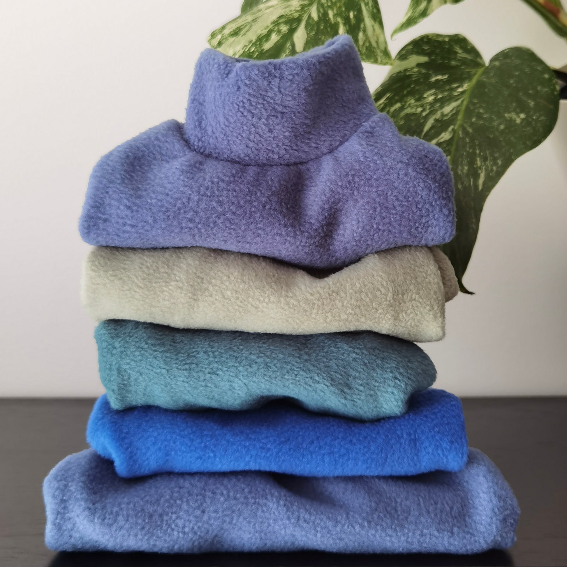 Stack of fleece dog sweaters in pigeon blue, aqua, teal and royal blue fleece from Lana Royals Pet Wear.